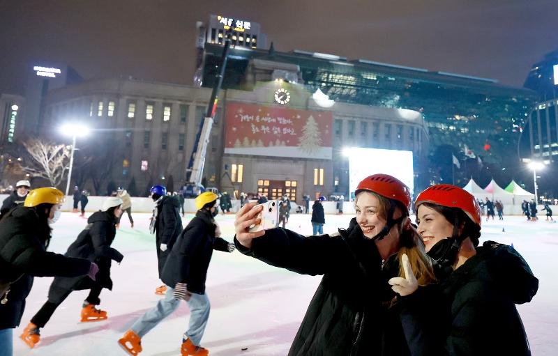 Dua orang asing terlihat sedang berfoto pada tanggal 21 Desember saat menikmati arena seluncur es yang berada di Alun-alun Seoul, Jung-gu, Seoul. (Yonhap News) 