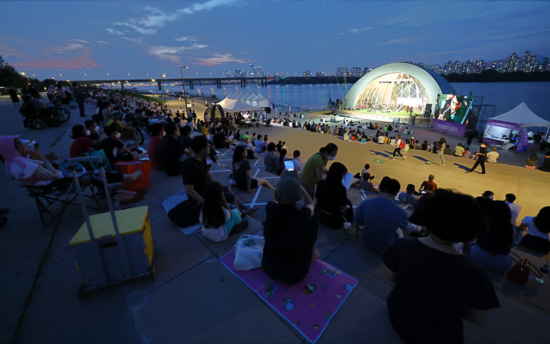 Festival Hangang pada musim panas diselenggarakan di delapan tempat yang berada di Taman Hangang dan di atas Sungai Hangang pada tanggal 4-20 Agustus. Foto di atas memperlihatkan para pengunjung yang sedang menikmati pertunjukan Hangang Summer Music Picnic pada tanggal 29 Juli 2022. (Yonhap News)