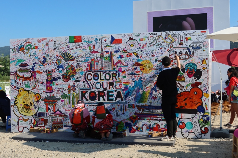 Para anggota pramuka dan pengunjung menulis pesan di coloring wall landmark pariwisata Korea pada tanggal 5 Agustus di Pusat Promosi Pariwisata Korea yang terletak di pintu masuk bumi perkemahan Jambore Pramuka Dunia Saemangeum tahun 2023. Coloring wall dengan tulisan Color Your Korea diisi dengan berbagai pesan dari para peserta jambore terkait< K-pop, pengalaman budaya, dan kesan pariwisata di Korea. 