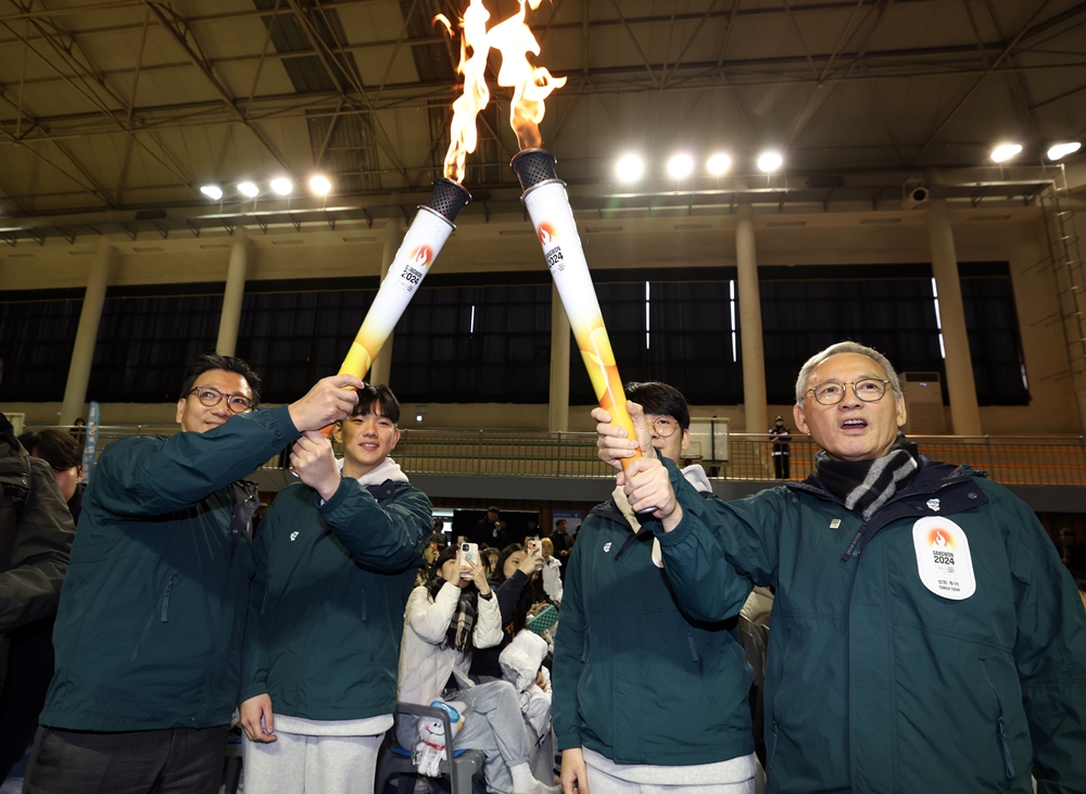 Menteri Kebudayaan, Olahraga, dan Pariwisata, Yu In Chon (pertama dari kanan) menerima api obor dari anggota IOC (Komite Olimpiade Internasional), Kim Jae Youl (pertama dari kiri) pada upacara penyalaan obor Olimpiade Remaja Musim Dingin Gangwon 2024 di Kota Wonju yang digelar pada tanggal 28 November di Gimnasium SMA Yukminkwan, Kota Wonju, Provinsi Gangwon.