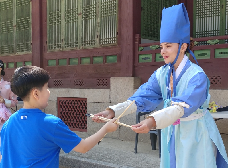 Foto di atas menunjukkan Sarah Shalaby yang sedang membantu seorang anak kecil yang ingin mencoba permainan tradisional Korea pada Festival Budaya Kerajaan yang digelar di depan Aula Gyeongchunjeon, Istana Changgyeonggung, Jongno-gu, Kota Seoul, Sarah berkata, Berbeda dengan Prancis, istana kuno dan musem di Korea bisa mudah dikunjungi dengan menggunakan transportasi umum. Mempelajari sejarah dan budaya di Korea sangat menarik karena banyak tempat bersejarah yang dibuka untuk umum. (Lee Kyoung Mi) 