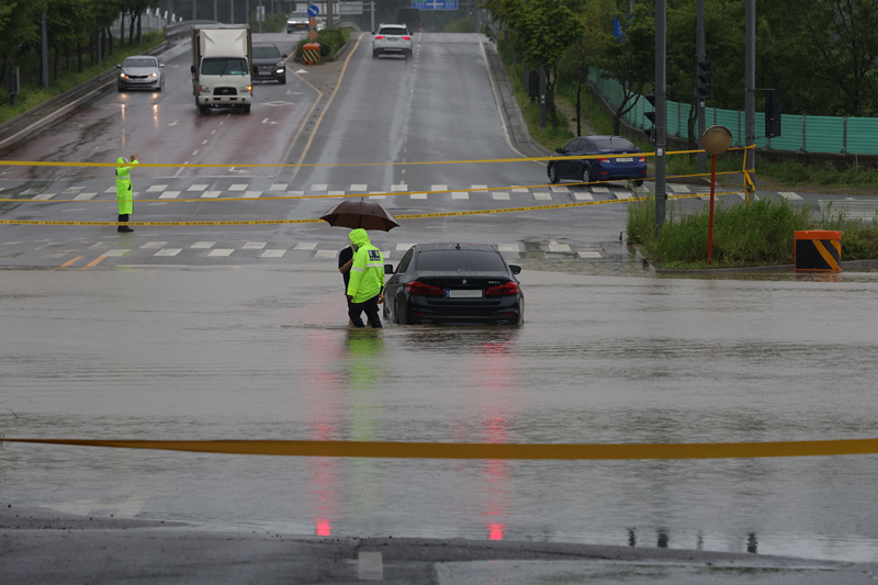 Mulai bulan Juli, pengemudi mobil bisa mengetahui risiko banjir di sekitar saat mengemudi mobil melalui aplikasi peta dan navigasi. Foto di atas menunjukkan polisi yang mengevakuasi pengemudi ke tempat yang aman setelah sebuah kendaraan terendam banjir di dekat Stasiun Munsan di Kota Paju, Provinsi Gyeonggi pada tanggal 18 Juli. (Yonhap News) 