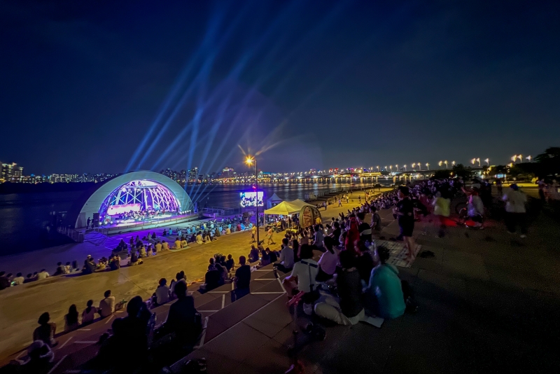 Festival Sungai Hangang 2024: Musim Panas akan diselenggarakan pada tanggal 26 Juli s/d 11 Agustus 2024 di atas perairan Sungai Hangang dan di sembilan Taman Hangang. Foto di atas menunjukkan warga Kota Seoul yang sedang menikmati pertunjukan Hangang Summer Music Picnic yang digelar di Taman Hangang Yeouido.  
