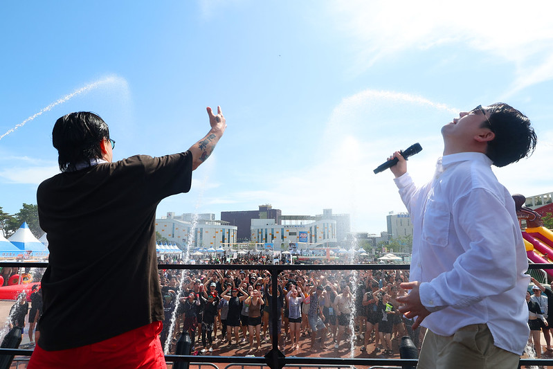 Para pengunjung bisa menikmati semburan air dan lumpur serta pertunjukan musik melalui panggung luar ruangan yang dipasang di zona umum Festival Lumpur Boryeong.  