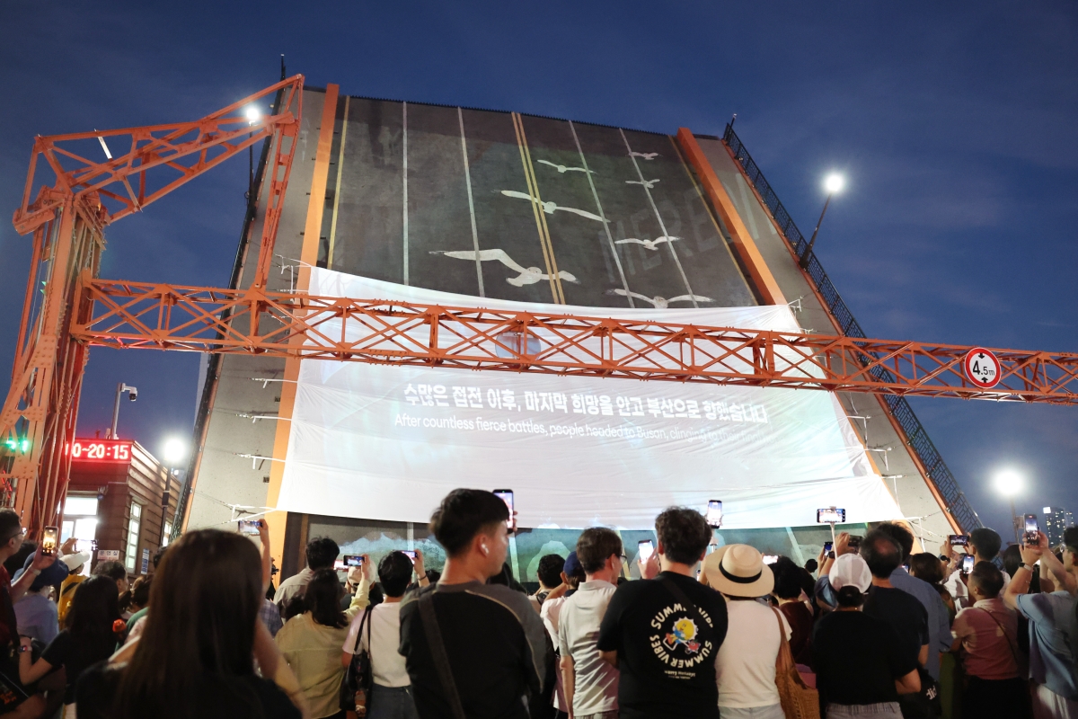Warga Busan berkumpul di Jembatan Yeongdodaegyo pada tanggal 25 Juli 2026 untuk menonton acara pengangkatan jembatan di kala malam dan penayangan video terkait kisah Busan saat menjadi ibu kota sementara Republik Korea selama 1.023 hari pada masa Perang Korea (1950-1953). Jembatan Yeongdodaegyo yang dibangun pada tahun 1932 merupakan jembatan pertama di Korea yang menghubungkan daratan dengan pulau. Jembatan tersebut saat ini menyambungkan area Jung-gu dan Yeongdo-gu di Busan. Lokasi tersebut juga menjadi salah satu lokasi simbolis di Busan sebagai tempat pertemuan dan perpisahan keluarga pada masa Perang Korea. 