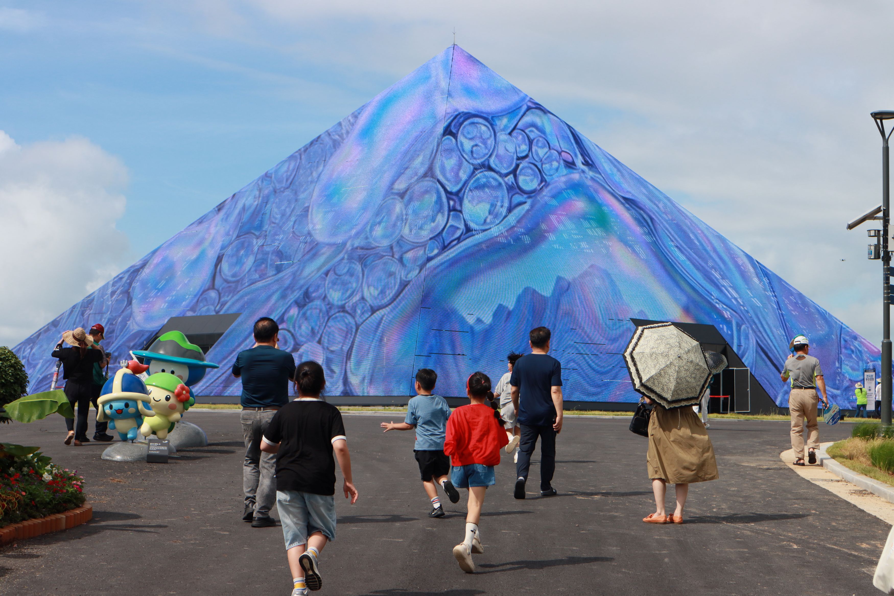 Sekitar sepekan menjelang pembukaan Pameran Pulau Dunia Yeosu 2026, acara pratinjau digelar pada 29 Agustus 2026 di lokasi utama pameran di Dolsan-eup, Kota Yeosu, Jeonnam-Gwangju. Foto memperlihatkan warga berjalan di depan fasad media Paviliun Pulau Tema. (Komite Penyelenggara Pameran Pulau Dunia Yeosu 2026)