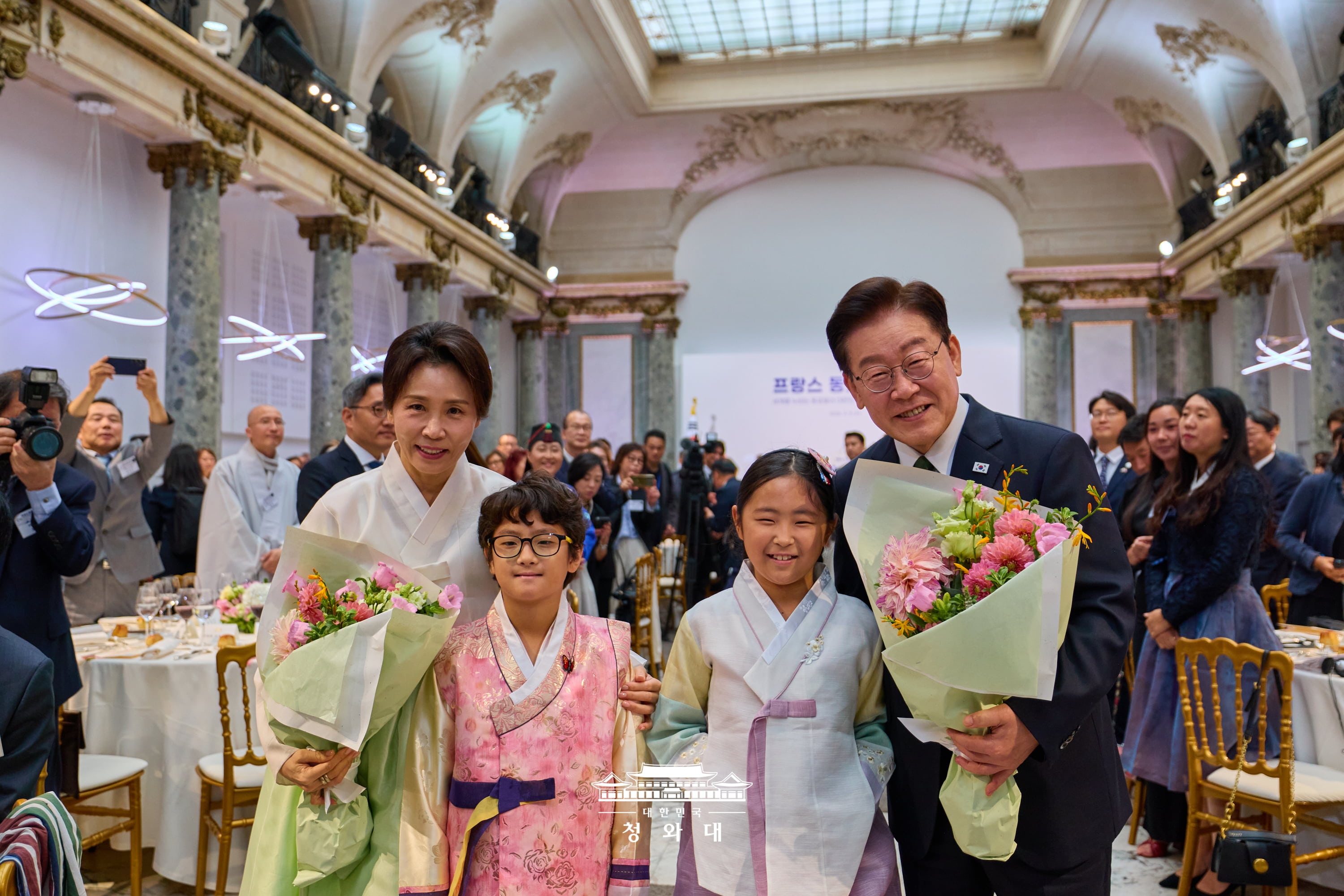 Presiden Lee Jae Myung dan Ibu Negara Kim Hea Kyung berfoto bersama sambil memegang buket bunga pemberian anak penyambut dalam pertemuan makan siang dengan diaspora Korea di Prancis yang digelar pada tanggal 9 September 2026 (waktu setempat) di Paris, Prancis. 
