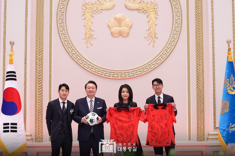 Presiden Yoon (kedua dari kiri) dan Ibu Negara Kim menerima hadiah berupa seragam timnas dan bola yang sudah ditandatangani para atlet timnas. Son Heung-min (pertama dari kanan) dan Lee Kang-in (pertama dari kiri) mewakili penyerahan hadiah pada jamuan makan malam timnas Korea yang diselenggarakan pada tanggal 8 Desember di Yeonbingwan, Cheong Wa Dae. (Kantor Kepresidenan Republik Korea)