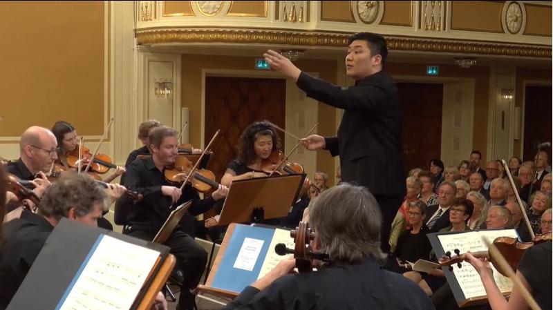 Yoon Hankyeol terlihat sedang memimpin sebuah orkestra pada konser babak final Herbert von Karajan Young Conductors Award yang digelar pada tanggal 6 Agustus (waktu setempat) di auditorium utama Mozarteum Foundation, Salzburg, Austria. (tangkapan layar situs resmi Festival Salzburg)
