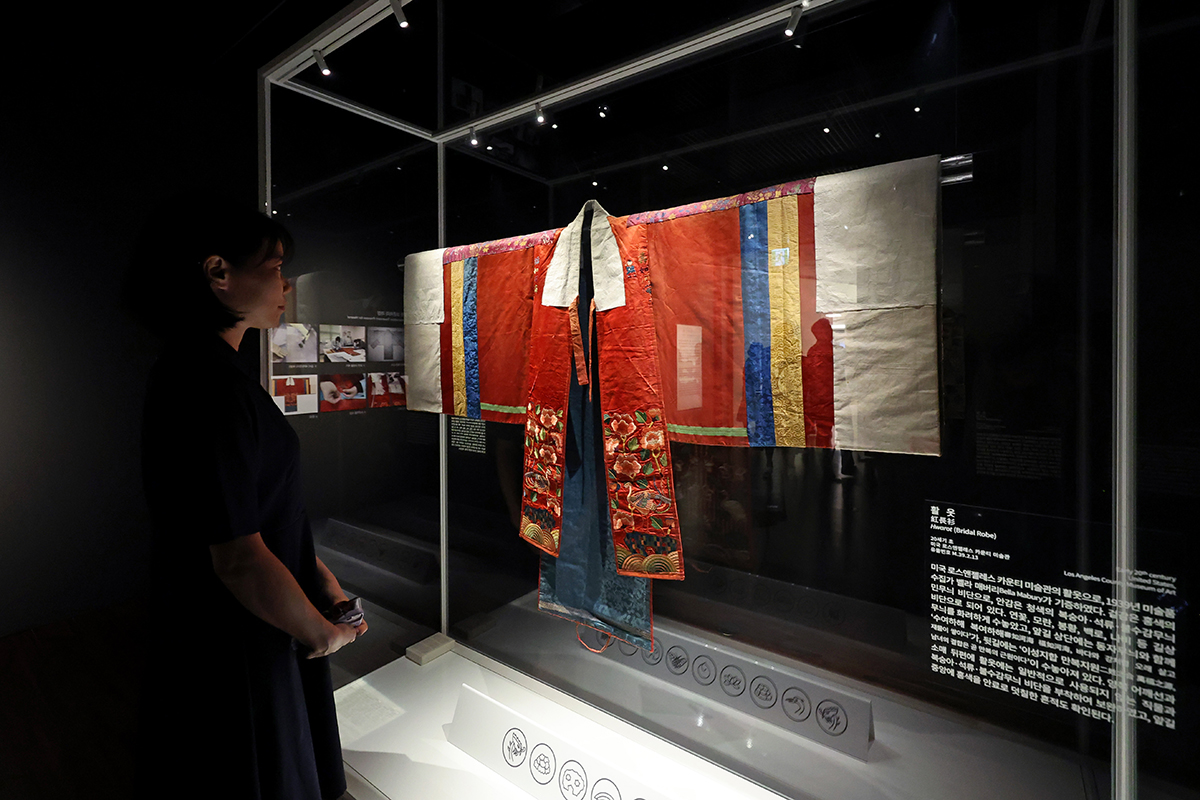 Seorang pengunjung sedang melihat hwarot pada pembukaan pameran khusus bertajuk Blooming Hwarot: Bridal Robes of the Joseon Royal Court untuk media yang digelar pada tanggal 13 September di National Palace Museum of Korea, Jongno-gu, Seoul. Hwarot adalah pakaian pengantin wanita yang dikenakan oleh para wanita bangsawan pada masa Dinasti Joseon. Pameran khusus tersebut akan berlangsung dari tanggal 15 September hingga 13 Desember dan memamerkan 110 artefak, termasuk sembilan potong hwarot. (Yonhap News)