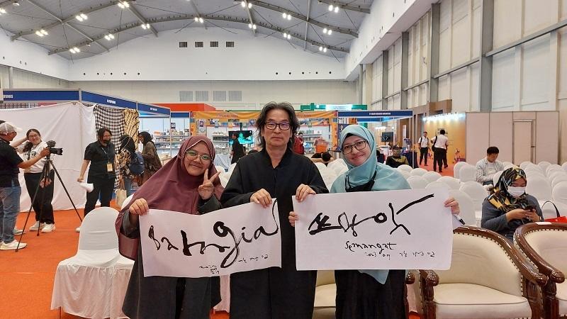 Penulis dan teman penulis berfoto bersama artis kaligrafi Kang Byung In dengan karya bertuliskan kata Bahagia dalam Bahasa Indonesia, dan kata Semangat yang dieja menggunakan Hangeul.