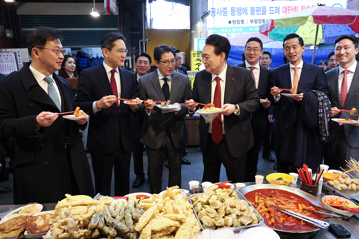 Presiden Yoon Suk Yeol terlihat sedang mencicipi tteokbokki bersama para pemimpin perusahaan besar Korea pada tanggal 6 Desember di Pasar Kkangtong, Jung-gu, Busan. Dari kiri ke kanan: Wakil Pimpinan Grup SK, Chey Jae-Won; Kepala Samsung Electronics, Lee Jae-yong; Pimpinan Grup Hyosung, Cho-Hyun-joon; Presiden Yoon Suk Yeol; Pimpinan Grup LG, Koo Kwang-mo; Wakil Pimpinan Grup Hanhwa, Kim Dong Kwan; dan Wakil Pimpinan HD Hyundai. (Yonhap News)