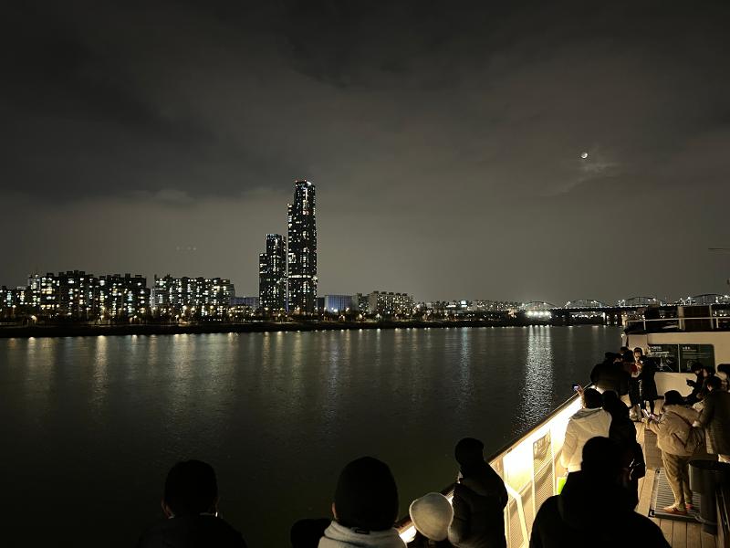 Pemandangan malam kota Seoul yang syahdu di bawah cahaya bulan yang terlihat dari dek kapal.