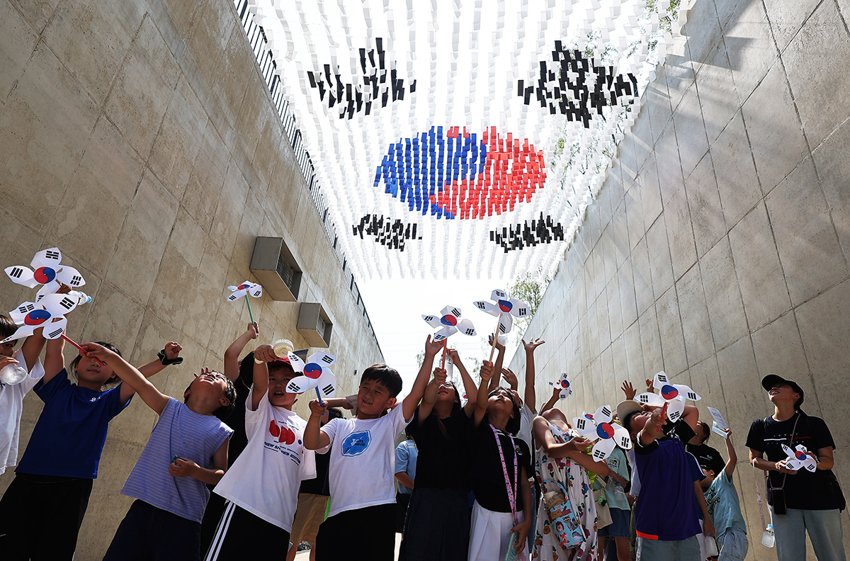 Pada tanggal 14 Agustus 2024 para siswa terlihat sedang melambaikan tangan sambil melihat taegeukgi (bendera nasional Korea) di Balai Peringatan Gerakan Kemerdekaan Hwaseong, Provinsi Gyeonggi. Hari tersebut merupakan sehari sebelum perayaan Hari Kemerdekaan Korea yang jatuh pada tanggal 15 Agustus. (Yonhap News)