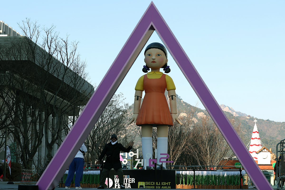 Seorang wisatawan asing terlihat sedang berfoto pada tanggal 18 Desember 2024 di depan Young-hee raksasa yang ditempatkan di tengah Alun-alun Gwanghwamun yang terletak di Jongno-gu, Seoul. Young-hee merupakan robot yang muncul dalam drama Squid Game dan memiliki peran dalam mengawasi para peserta yang bergerak selama permainan lampu merah lampu hijau. (Lee Jun Young)