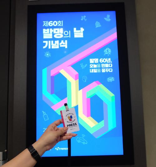 Tanda pengenal PRESS resmi dari Wartawan Kehormatan Korea.net ditunjukkan di depan layar digital yang menampilkan poster acara Hari Penemuan ke-60. (Aditya Nurmalita Pervitasari) 
