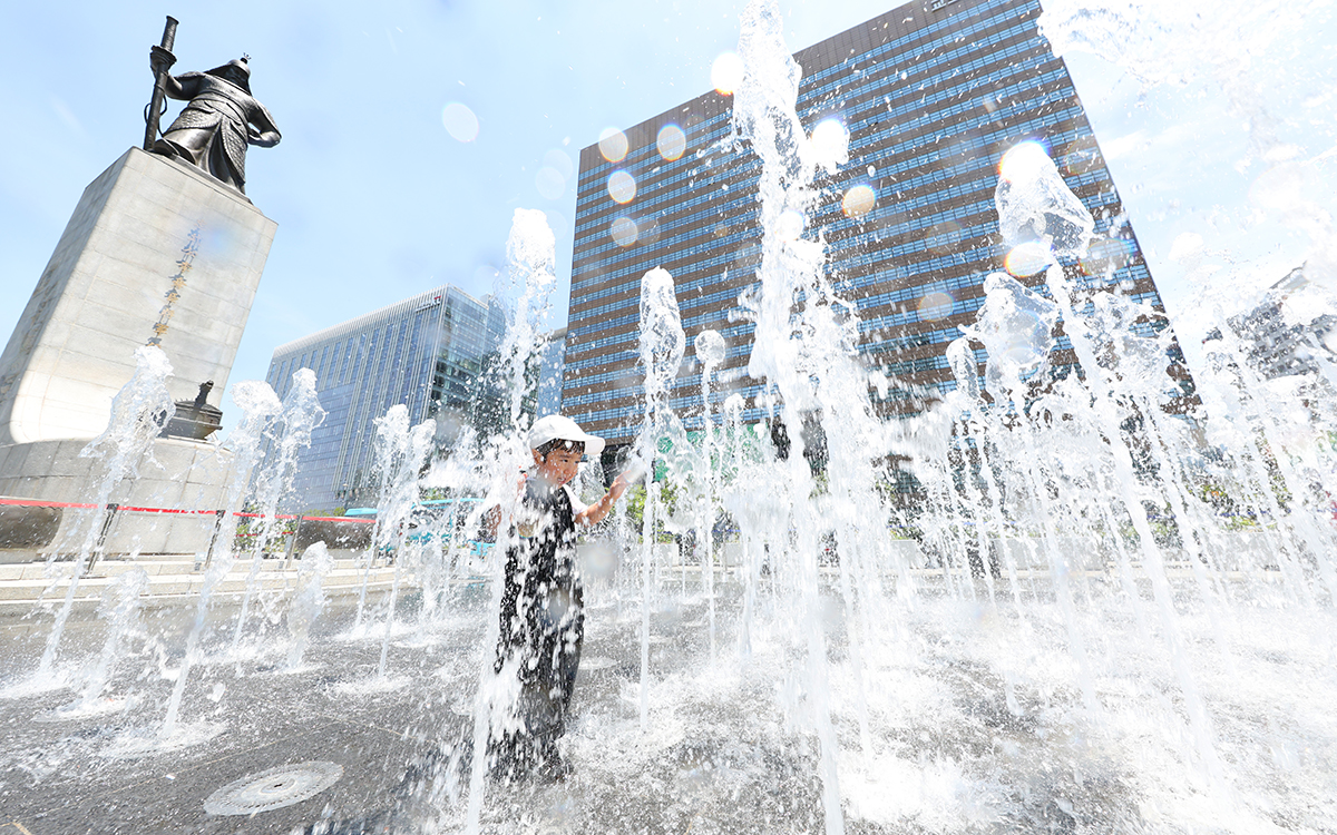 Seorang anak terlihat sedang bermain di air mancur lantai di depan patung Jenderal Yi Sun-sin di Jongno-gu, Seoul pada tanggal 12 Juni 2025. Pada hari itu, suhu tertinggi di siang hari di Seoul melonjak hingga 31 derajat Celsius. (Lee Jeong Woo)