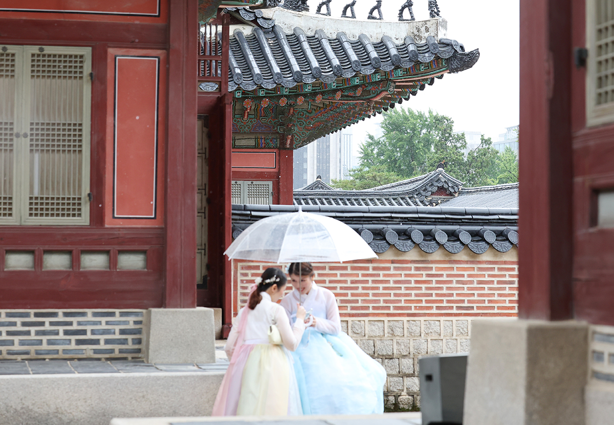 Dua orang wisatawan asing terlihat memakai payung saat mengunjungi Istana Gyeongbokgung di Seoul pada tanggal 20 Juni 2025. Hari itu hujan turun lebat di seluruh penjuru Korea untuk menandai mulainya periode jangma, yaitu musim hujan di tengah musim panas. (Lee Jeong Woo)
