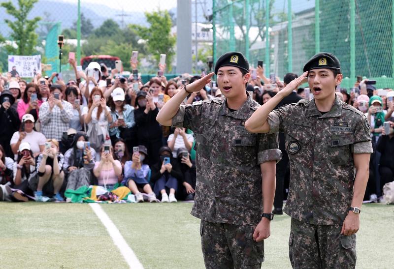 Anggota BTS RM (kiri) dan V terlihat sedang memberikan salam kepada para penggemar dan jurnalis pada tanggal 10 Juni 2025 dalam sebuah acara yang menandai pelepasan tugas militer mereka. Acara tersebut digelar di taman olahraga di Sinbuk-eup, Chuncheon, Provinsi Gyeonggi. (Yonhap News)