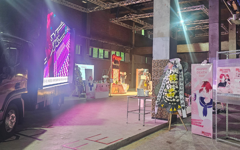 Area masuk K-pop Funeral Café dipenuhi dengan spanduk, truk protes, dan karangan bunga dengan ucapan selamat tinggal. 