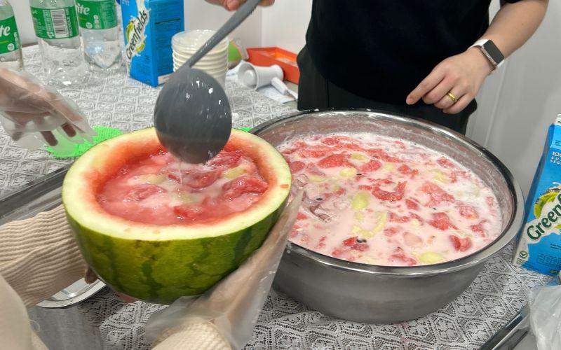 Panitia menuangkan hwachae yang telah diracik dengan es batu, susu, soda, dan susu kental manis ke dalam wadah semangka yang sudah disendok. 