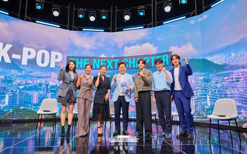 Presiden Lee Jae Myung terlihat sedang berfoto dengan para peserta pada tanggal 20 Agustus 2025 di acara K-Pop: The Next Chapter di Arirang TV. Dari kiri ke kanan adalah anggota grup K-pop TWICE Jeongyeon dan Jihyo; sutradara KPop Demon Hunters Maggie Kang; Presiden Lee; produser musik sekaligus DJ R.Tee; kritikus musik Kim Young-dae; serta pembawa acara Jang Sung-kyu.