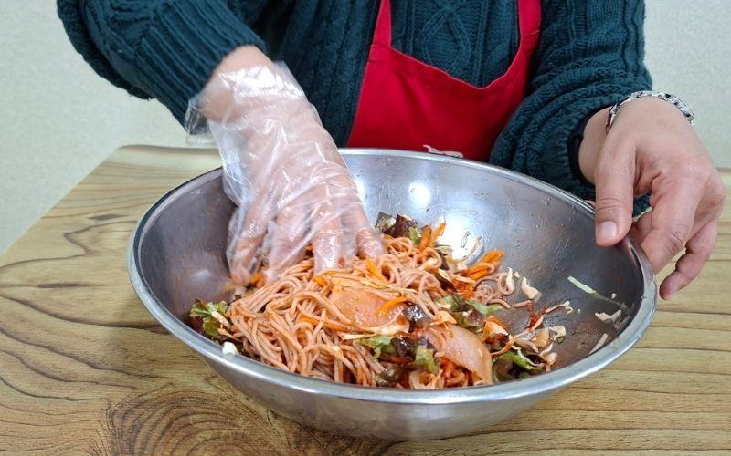 Proses mencampur mi makguksu yang telah matang dengan bumbu untuk membuat bibim makguksu. 