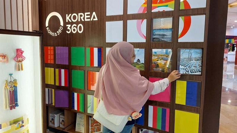 Penulis berfoto di papan putar bergambar macam-macam unsur budaya Korea yang menjadi bagian dalam permainan. (Maulia Resta Mardaningtias)