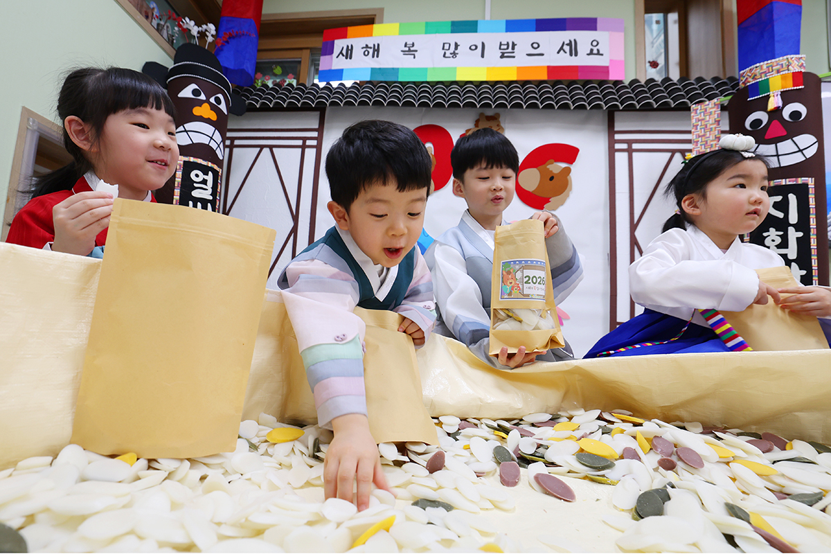 Anak-anak kecil berpakaian hanbok terlihat sedang mengumpulkan tok untuk dimasukkan ke dalam bungkusan pada tanggal 13 Februari 2026 di PAUD Samjeon Chorok, Songpa-gu, Kota Seoul. 
