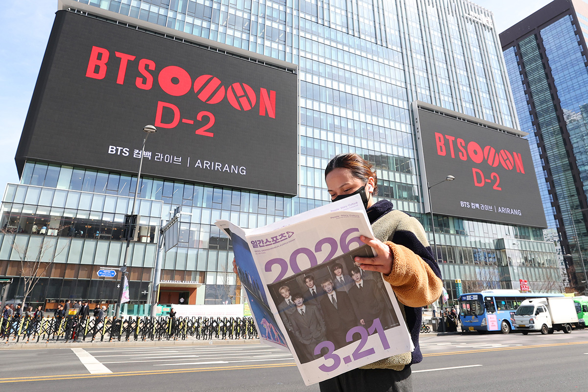  Seorang penggemar BTS membaca isi sebuah koran yang halaman depannya dipenuhi dengan foto anggota BTS. Potret tersebut diambil pada tanggal 19 Maret 2026 di depan gedung KT Gwanghwamun yang berada dekat dengan lokasi konser BTS, yaitu Alun-alun Gwanghwamun, Jongno-gu, Kota Seoul. (Lee Jeong Woo)