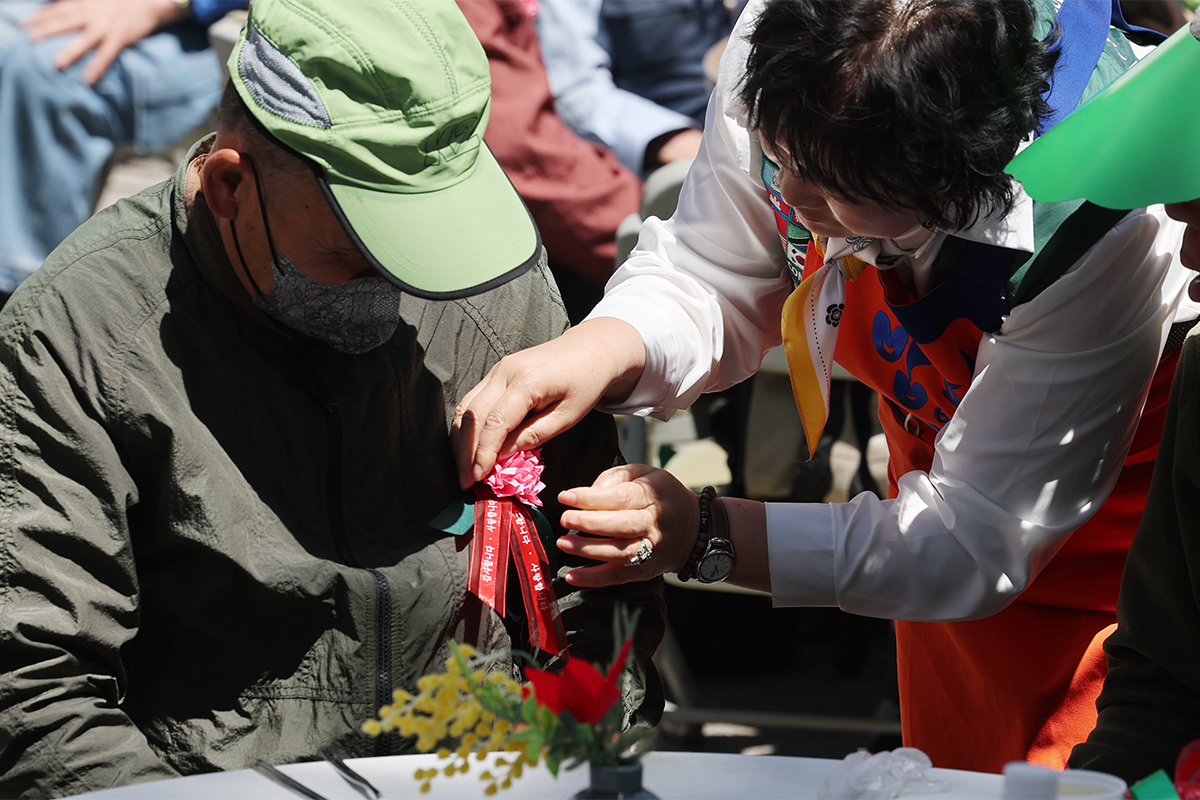 Seorang relawan menyematkan pin bunga anyelir ke baju seorang lansia pada tanggal 8 Mei 2026 di Kantor Pusat Berbagi Makanan yang terletak di Dongdaemun-gu, Seoul. Tanggal 8 Mei setiap tahunnya dirayakan sebagai Hari Orang Tua sehingga warga biasanya memberikan bunga anyelir ke orang tua masing-masing maupun lansia di sekitar mereka. (Yonhap News)