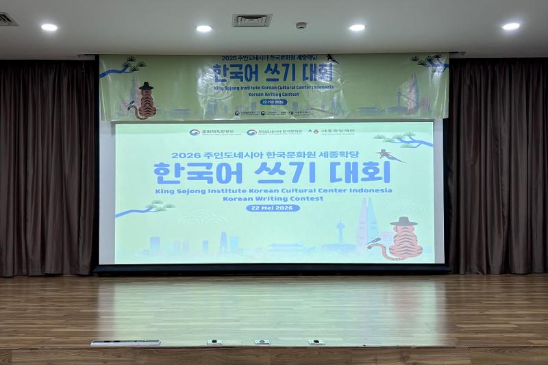 Layar proyektor yang menampilkan poster Kontes Menulis Bahasa Korea KSI KCCI 2026. 