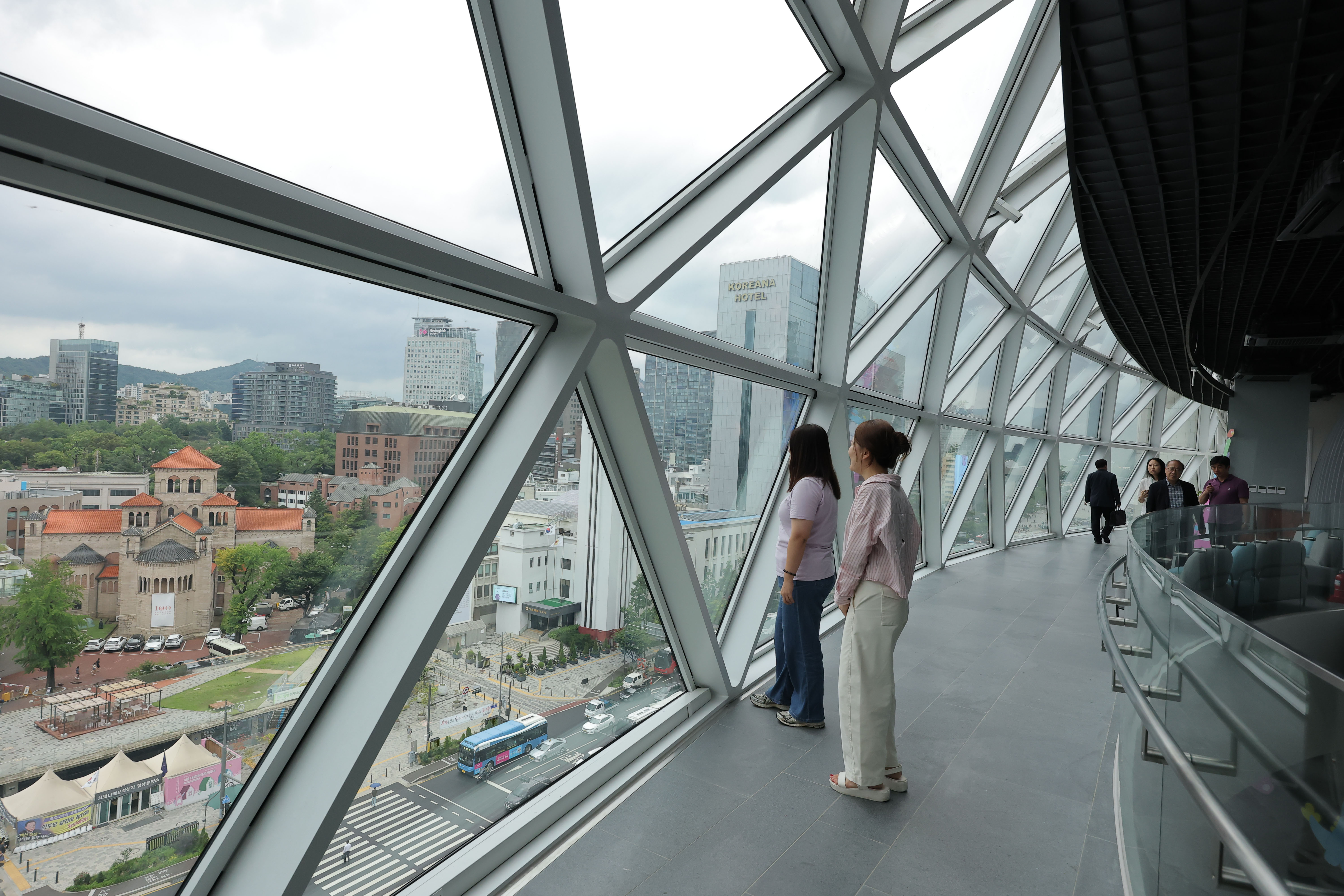 Para warga terlihat sedang melihat pemandangan kawasan Sejong-daero di Sky Observatory pada tanggal 6 Juli 2026. Tempat tersebut baru dibangun di lantai 8 dan 9 Gedung Barat Balai Kota Seoul. (Yonhap News)