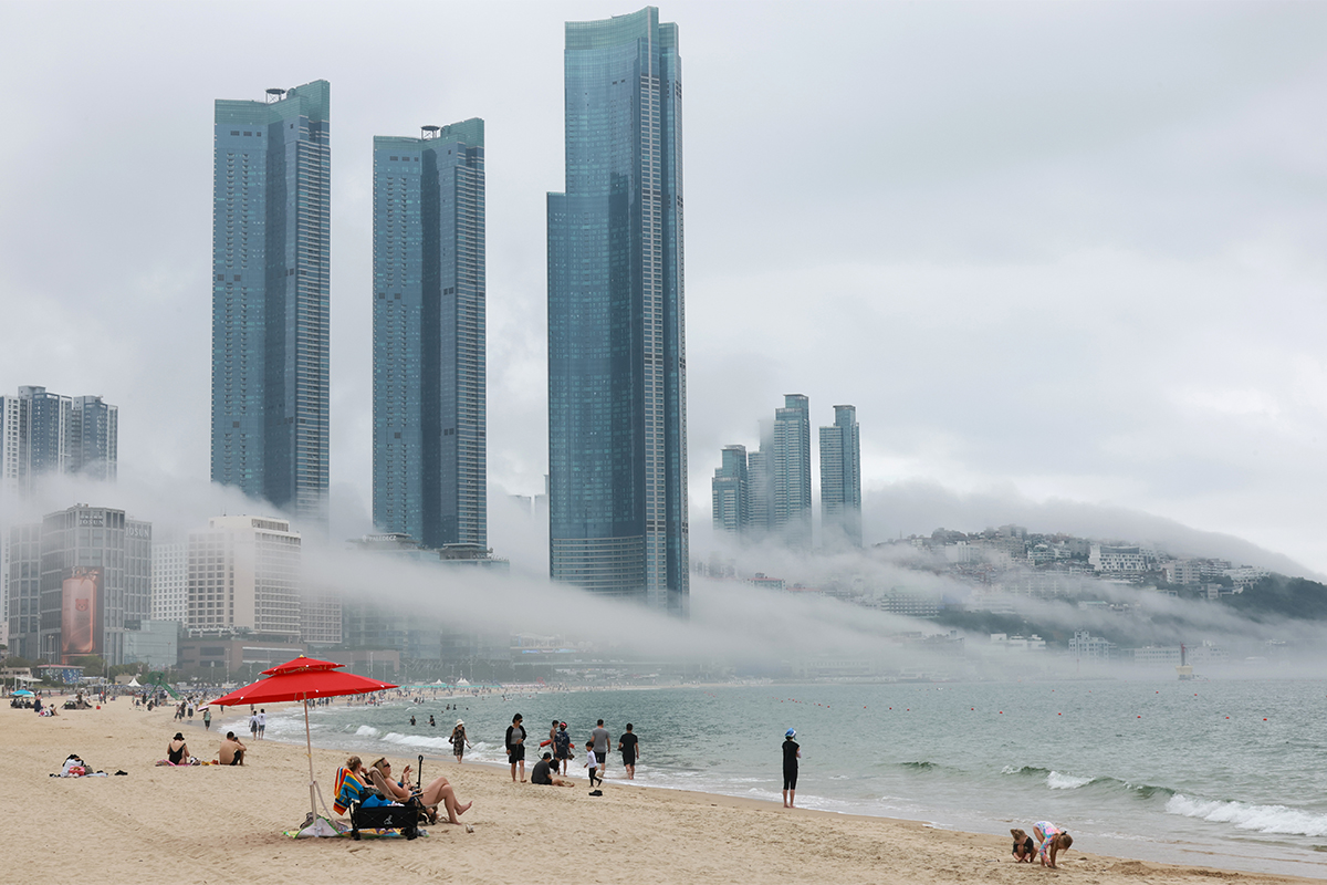 Kabut laut terlihat membentang di sepanjang garis pantai Haeundae, Busan, pada tanggal 7 Juli 2026, menciptakan pemandangan yang unik. Meski cuaca mendung, warga dan wisatawan tetap datang ke pantai untuk bermain air dan berjalan-jalan sambil menikmati suasana pantai di musim panas. (Yonhap News)