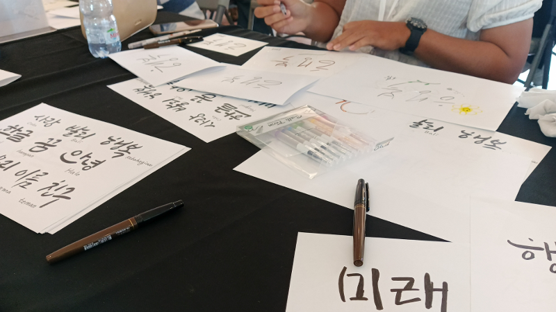 Peserta yang sedang berlatih mencoba berbagai gaya penulisan hangeul menggunakan perlengkapan menulis yang telah disediakan pada acara Sentuhan Hangeul di Ujung Jari yang digelar pada tanggal 20 Juni 2026 di Konsulat Republik Korea di Bali. 