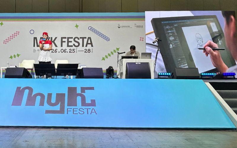 Ju Dong-geun menggambar secara langsung di atas panggung saat sesi MyK Voice berlangsung sambil menjawab pertanyaan dari pemandu acara, komedian Lee Eun-ji, pada hari Sabtu (27/6/2026) di KINTEX. 