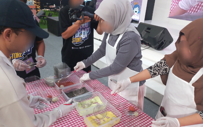 Peserta menggulingkan tok ke dalam berbagai pilihan taburan bubuk kacang dan bubuk remahan kastela yang diberi warna pada sesi terakhir pembuatan gyeongdan yang dilaksanakan pada tanggal 13 Juli 2026 di area Grand Atrium & Mosaic Walk, Kota Kasablanka Mall, Jakarta.  