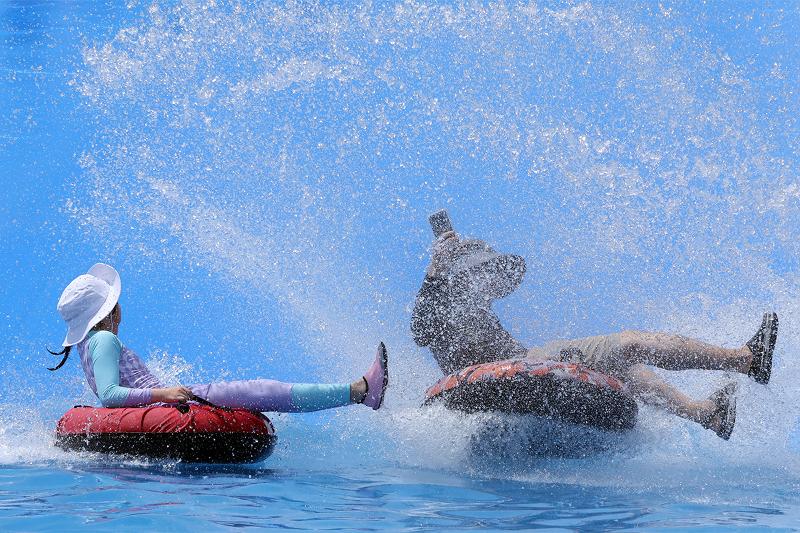 Para pengunjung terlihat sedang menikmati seluncuran air menggunakan ban pelampung di taman bermain air anak-anak Samnak Ecological Park, Sasang-gu, Busan, pada tanggal 21 Juli 2026, sambil menyegarkan diri di tengah cuaca panas yang terus berlanjut. (Yonhap News)