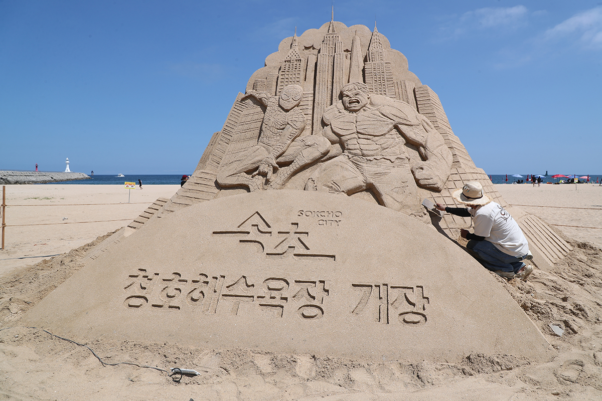Seorang pematung pasir terlihat sedang mengerjakan patung pasir Spiderman dan Hulk pada tanggal 5 Agustus 2026 di Pantai Cheongho, Kota Sokcho, Provinsi Gangwon. (Yonhap News)