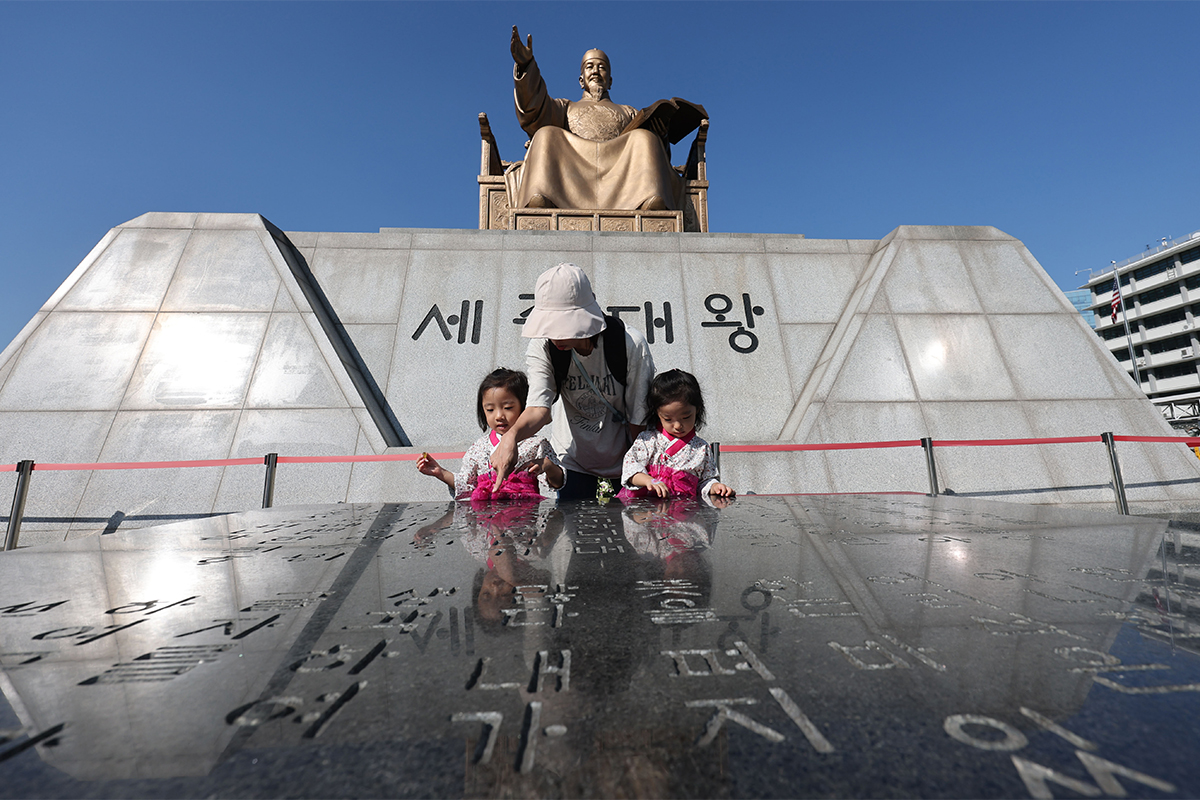 Sehari menjelang peringatan 100 tahun penetapan Hari Hangeul, sebuah keluarga mengamati lempengan batu yang memuat kata pengantar Hunminjeongeum di depan patung Maharaja Sejong di Alun-alun Gwanghwamun, Seoul, pada tanggal 8 Oktober 2026. (Yonhap News)